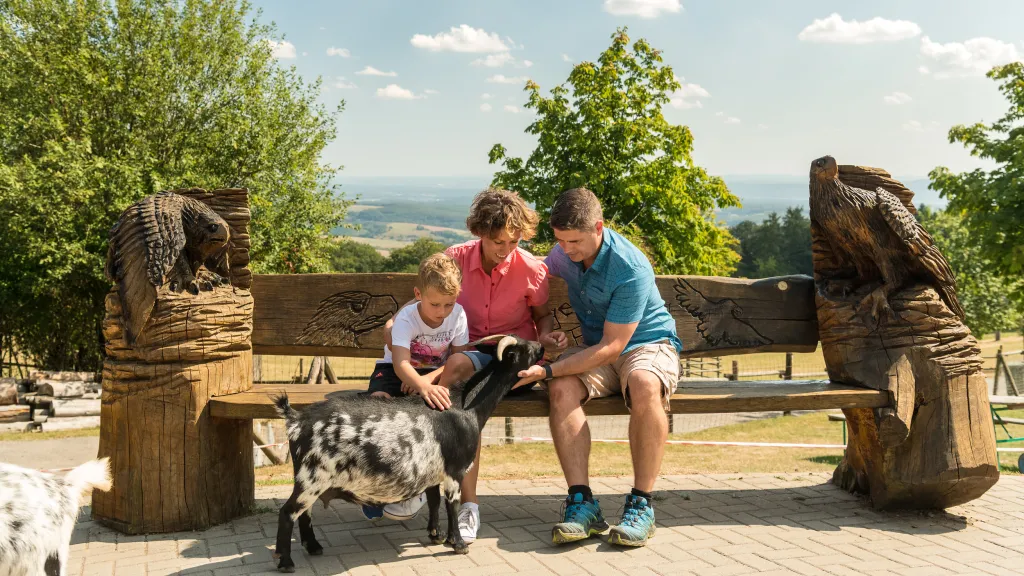 Eine Familie sitzt beim Wildpark Potzberg auf einer Bank und streicheln eine Ziege.