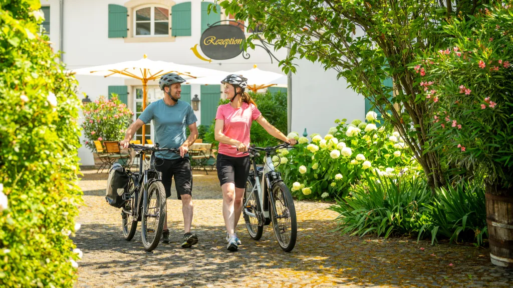 Zwei Personen schieben ihre Fahrräder aus einer Unterkunft in der Pfalz und starten zu eine Radtour.
