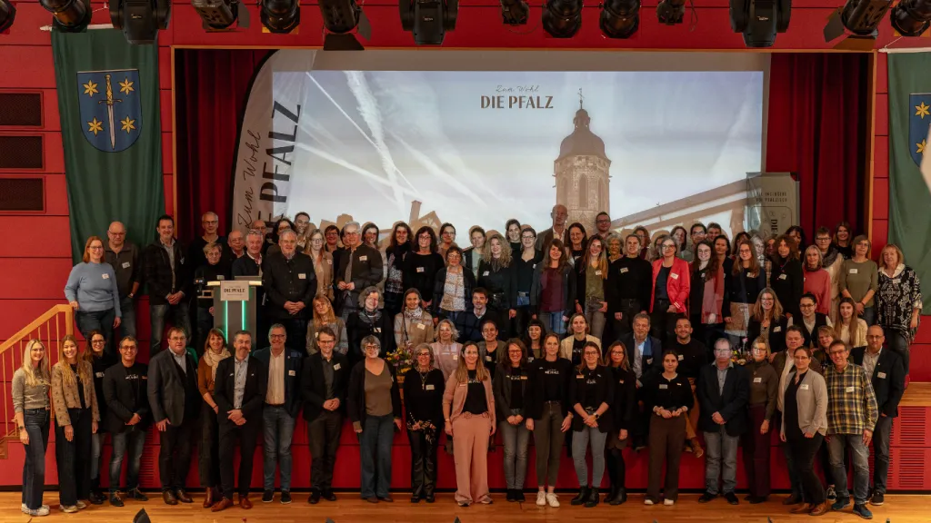 Die Teilnehmenden des 4. Tourismustages Pfalz in Kandel stehen alle vor der Bühne und lächeln in die Kamera
