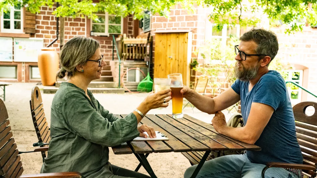 Zwei Personen sitzen im Naturfreundehaus Elmstein und genießen ein kühles Getränke.