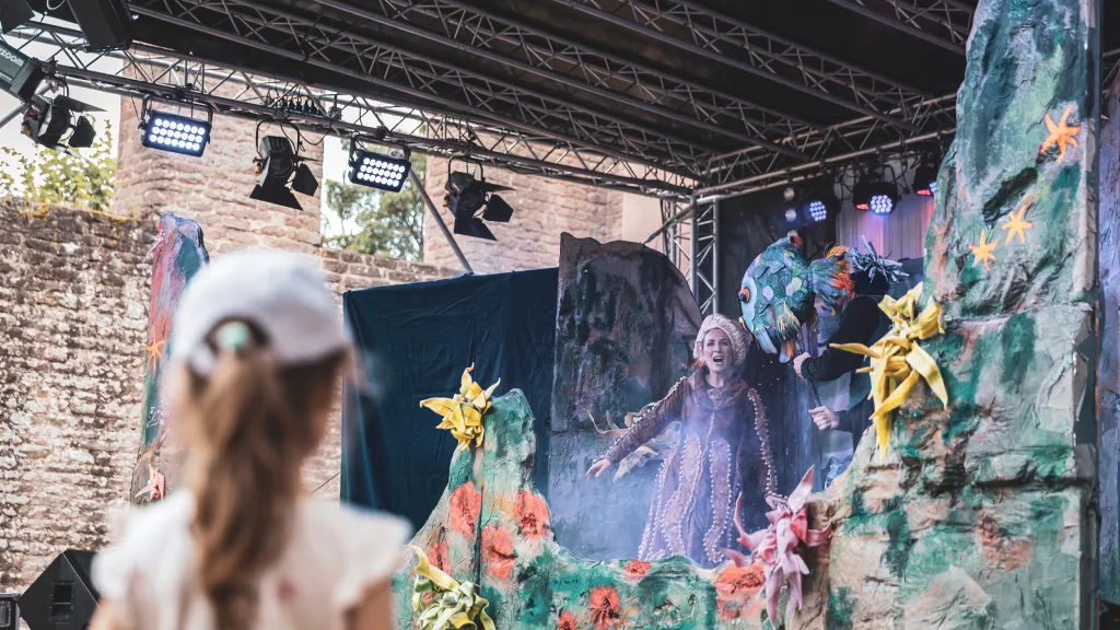 Ein Kind steht vor einer Bühne und betrachtet ein Theaterstück.