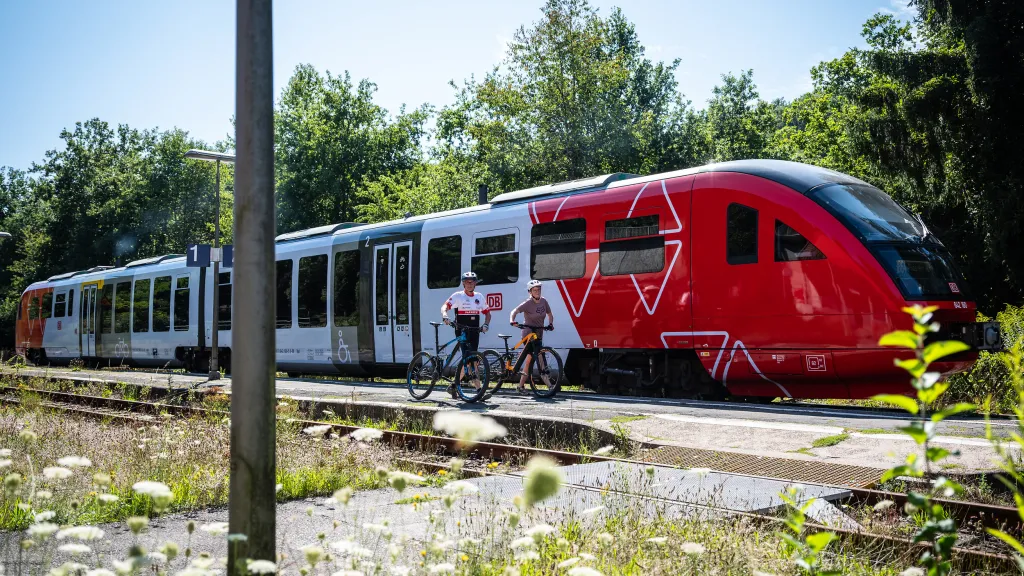 Zwei Personen mit Mountainbike spazieren entlang eines Bahnhofes