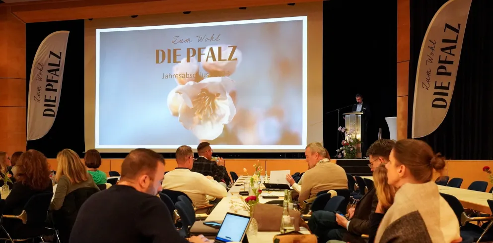 Blick auf eine Bühne mit Präsentation Zum Wohl die Pfalz im Vordergrund Zuschauer