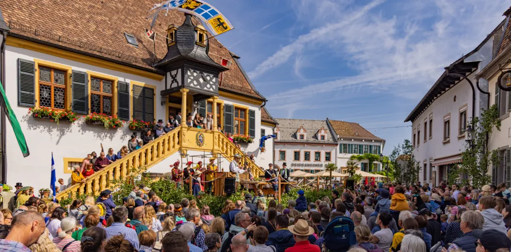 Menschen schauen bei der historischen Geißbockversteigerung in Deidesheim zu. 