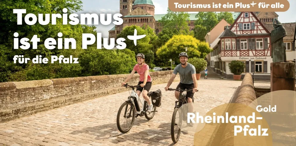Zwei Personen fahren mit dem Rad über eine Brücke nahe des Speyerer Doms. Der Bildtext lautet: Tourismus ist ein Plus für die Pfalz - Rheinlandpfalz Gold