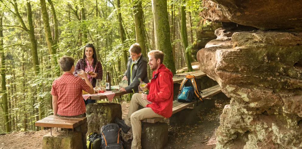 Eine Familie macht am Rastplatz vor einem Sandsteinfelsen im Pfälzerwald rast.