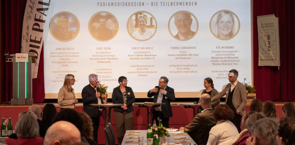 Sechs Personen stehen bei einer Podiumsdiskussion des Tourismustages Pfalz vor der Bühne.