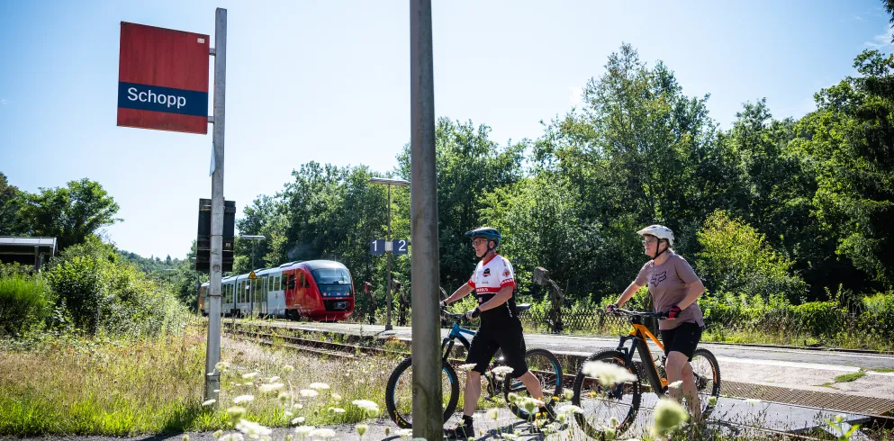 Zwei Personen mit ihren Mountainbikes am Bahnhof Schopp. 