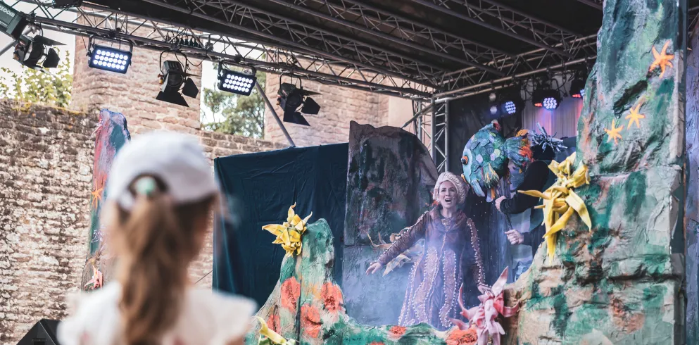 Ein Kind steht vor einer Bühne und betrachtet ein Theaterstück.