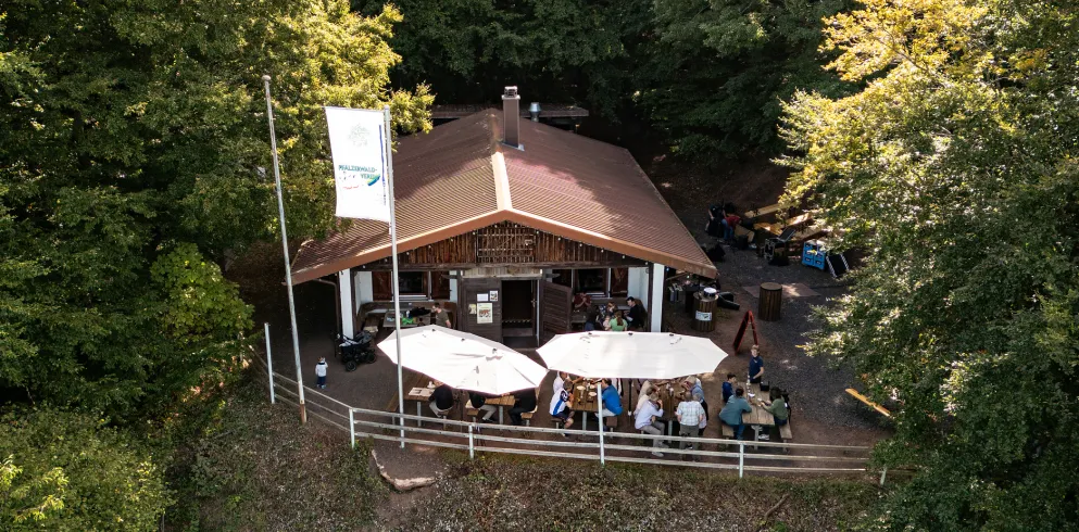 Menschen sitzen im Außenbereich der Hohlsteinhütte und genießen ein Gericht und etwas zu Trinken. 