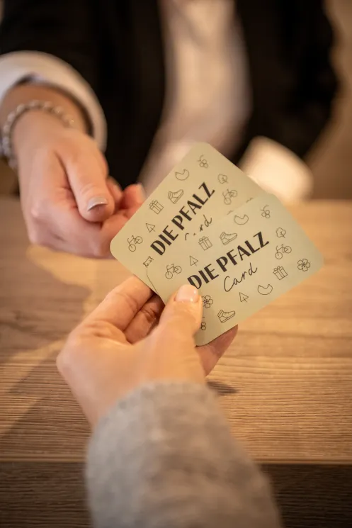 Eine Person reicht einer anderen Person zwei Karten auf denen "Die Pfalzcard" steht.