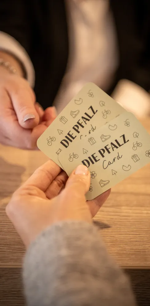 Eine Person reicht einer anderen Person zwei Karten auf denen "Die Pfalzcard" steht.