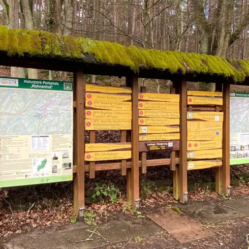 Ein Informationsschild im Wald mit mehreren Tafeln. Die Tafeln enthalten Karten und Hinweise für Wanderer.