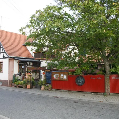 Ein charmantes Gebäude mit einem roten Zaun und einer begrünten Eingangstür. Die Straße ist ruhig und von Bäumen gesäumt.