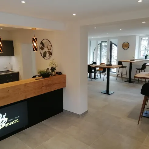 Ein modernes Café mit einer einladenden Theke aus Holz. Die helle Innenausstattung bietet Platz für mehrere Tische und Stühle.