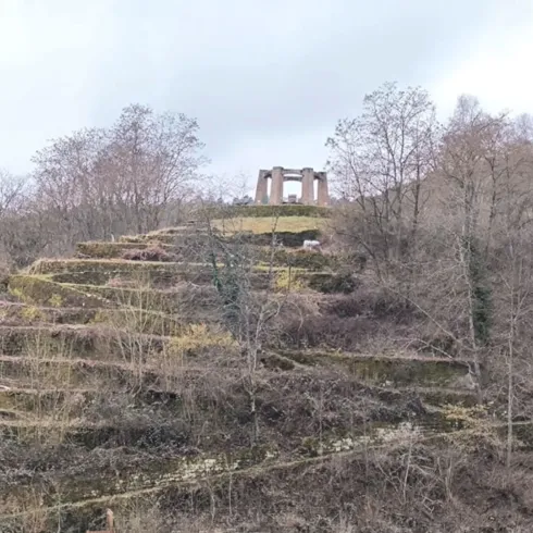 Eine grüne Hügellandschaft mit den neu angelegten Obstterassen und herbstlichen Bäumen. Oben auf dem Hügel steht eine historische Ruine, das Kriegerdenkmal von Weidenthal.