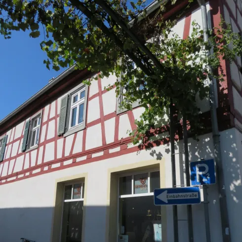 Ein charmantes Fachwerkhaus mit grünen Fensterläden und einem Parkplatzschild. Die Fassade ist hell mit roten und weißen Mustern.