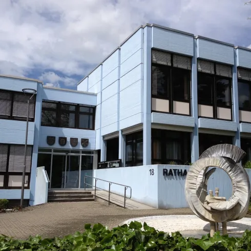 Ein modernes, blaues Gebäude mit großen Fenstern. Vor dem Eingang steht eine elegante Skulptur.