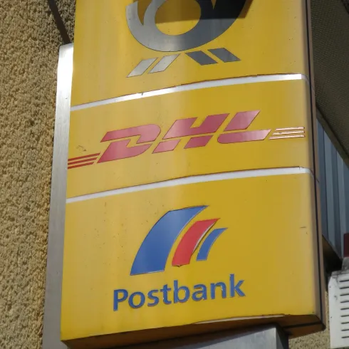 Ein gelbes Schild mit dem Logo von DHL und der Postbank. Die Schrift ist klar sichtbar und gut lesbar.