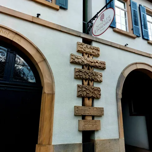 Ein historisches Gebäude mit einem dekorativen Holzschild. Die Fenster sind mit blauen Läden versehen.