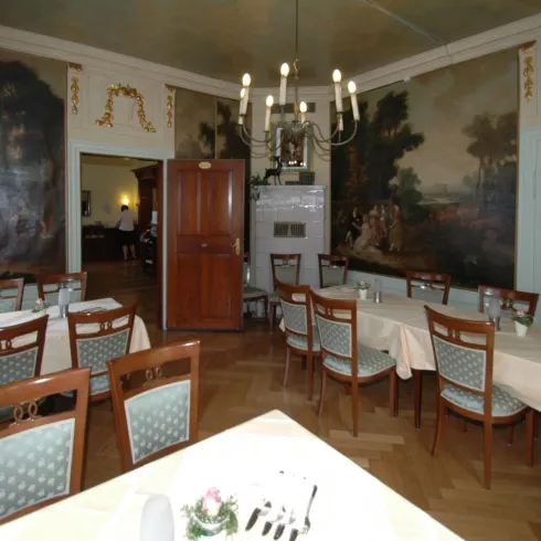 Ein eleganter Speisesaal mit mehreren Tischen und schönen Wandmalereien. Der Raum hat eine gemütliche Atmosphäre und ist mit einer schöner Deckenleuchte ausgestattet.