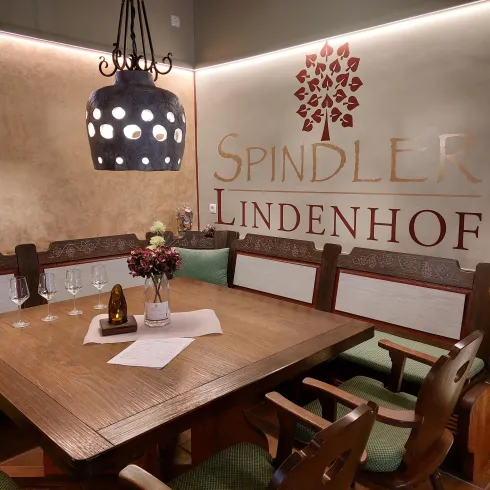Ein gemütlicher Essbereich mit einem großen Holztisch und traditionellen Stühlen. An der Wand steht der Name "Spindler Lindenhof" mit einem dekorativen Baum.