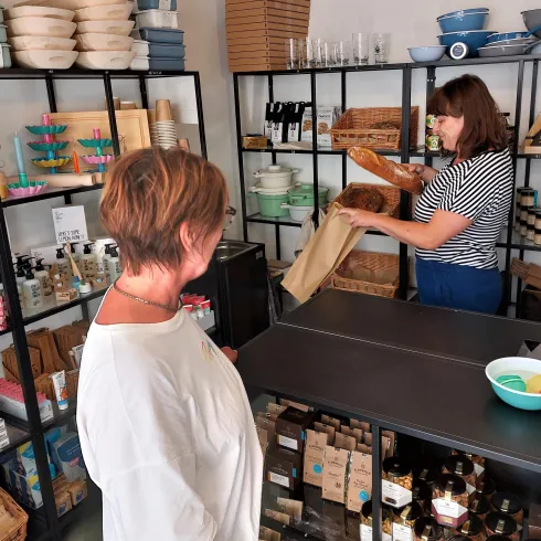 In einem Geschäft stehen zwei Frauen. Eine Verkäuferin packt Produkte in Papier, während die Kundin zusieht.