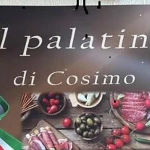 Ein Schild mit dem Schriftzug "il palatino di Cosimo". Im Hintergrund sind verschiedene Wurst- und Käseprodukte sowie Gemüse zu sehen.