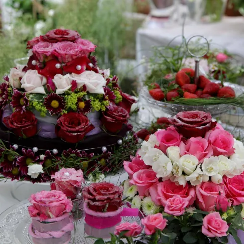 Ein wunderschöner Tisch mit üppigen Blumenarrangements in verschiedenen Rosatönen. Im Mittelpunkt stehen kunstvoll dekorierte Torten aus Blumen.