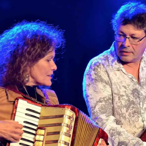 Ein Duo mit einer Frau am Akkordeon und einem Mann am Kontrabass spielt auf einer Bühne. Die Beleuchtung ist blau und schafft eine festliche Atmosphäre.