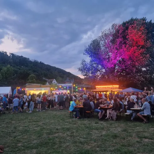 Eine lebhafte Veranstaltung im Freien mit vielen Menschen. Bunte Lichter und Stände schaffen eine festliche Atmosphäre.