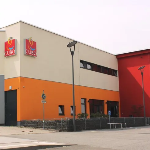 Ein modernes Gebäude mit bunten Außenwänden in Orange und Rot. An der Fassade befinden sich die Schilder des Unternehmens "CUBO".