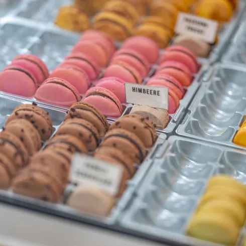 Bunte Macarons in verschiedenen Geschmacksrichtungen, angeordnet in einer Vitrine. Die Farben reichen von rosa und gelb bis zu braun und orange.
