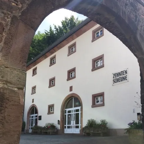 Ein historisches Gebäude mit einer weißen Fassade und mehreren Fenstern. Der Eingang ist von einem steinernen Bogen umrahmt.