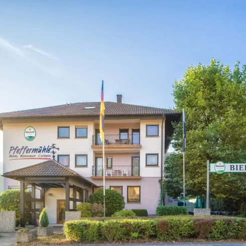 Ein einladendes Gebäude mit einem Restaurant und einem Biergarten. Umgeben von grünen Bäumen und einem klaren Himmel.
