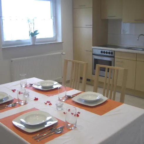 Ein eleganter Essbereich mit einem dekorierten Tisch und Geschirr. Im Hintergrund ist eine moderne Küche sichtbar.