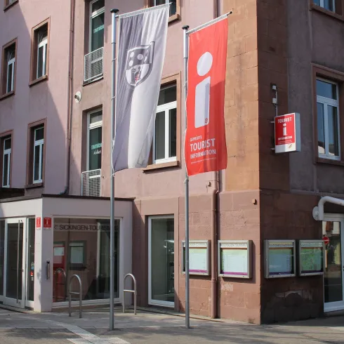 Ein modernes Gebäude mit Fahnen und Werbeschildern. Der Eingangsbereich ist gut sichtbar und einladend.