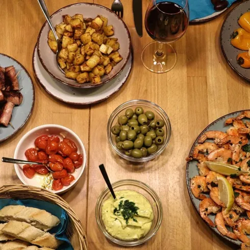 Ein erfreuliches Festmahl mit gegrilltem Fleisch, Garnelen, Oliven und gebratenen Kartoffeln. Dazu gibt es frisches Brot und Wein auf einem Holztisch.
