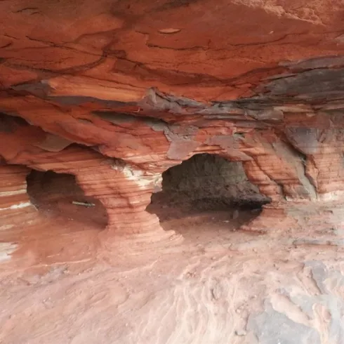 Eine interessante Höhle mit rötlichen Felsen und kleinen Durchgängen. Die texturierten Wände zeigen die natürlichen Formationen der Landschaft.