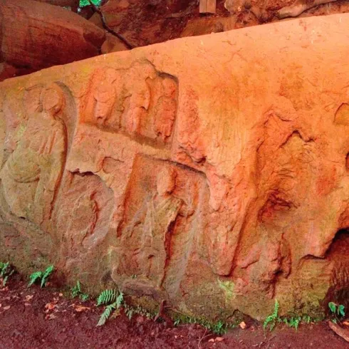 Ein großer, bearbeiteter Stein mit alten Schnitzereien. Die umgebende Natur ist grün und bewaldet.