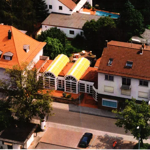 Ein Überblick auf ein Wohngebiet mit mehreren Häusern. Eines der Gebäude hat ein auffälliges, gelbes Glasdach.