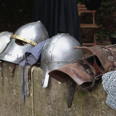 Ein Steinsockel, auf dem  mehrere mittelalterliche Ritterhelme und Rüstungsteilen.