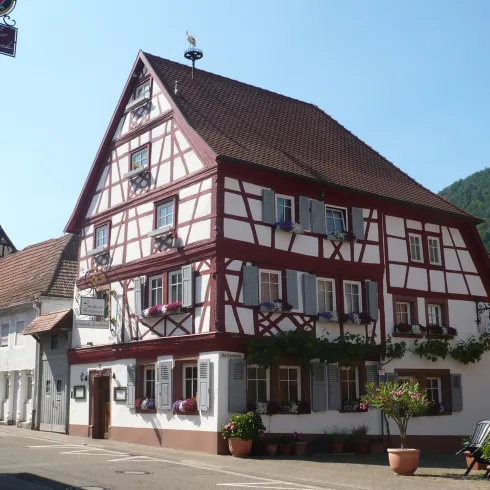 Ein traditionelles Fachwerkhaus mit rotem Rahmen und weißen Wänden. Im Vordergrund sind Blumen und Pflanzen zu sehen.