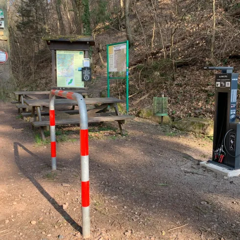 Ein Wanderweg mit Informationen, einem Tisch und einer Bank. Neben dem Weg steht eine Ladestation für E-Bikes.