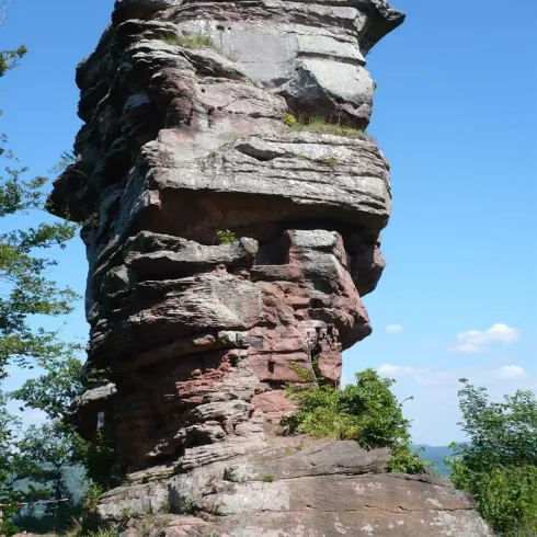 Ein großer, beeindruckender Felsen steht vor einem klaren blauen Himmel. Grüne Pflanzen wachsen an den Seiten des Felsens.
