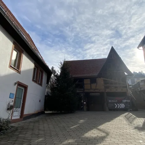 Ein kleiner Innenhof mit zwei Gebäuden, einem modernen und einem traditionellen Fachwerkhaus. Der Himmel ist bewölkt und die Umgebung wirkt ruhig und einladend.