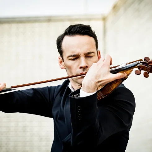 Ein Mann spielt leidenschaftlich Violine. Er trägt einen Anzug und konzentriert sich auf seine Musik.