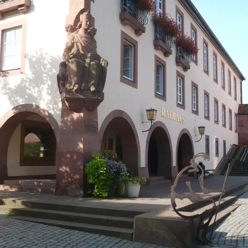 Ein historisches Gebäude mit einer Statue und bunten Blumenkästen. Die Umgebung ist gepflastert und gut beleuchtet.