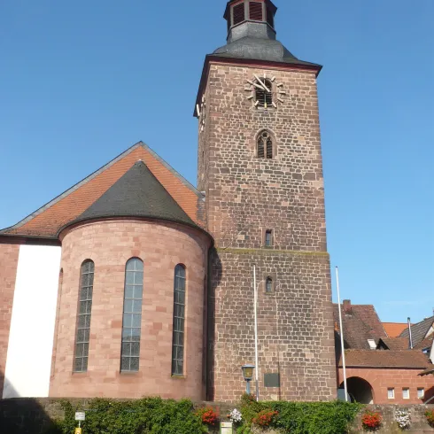 Eine alte Kirche mit einem hohen Glockenturm und einem runden Anbau. Der Himmel ist klar und blau.