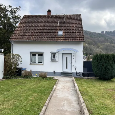 Ein gemütliches Einfamilienhaus mit einem gepflegten Garten. Im Hintergrund sind sanfte Hügel sichtbar.